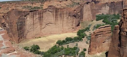 A panoramic view of a canyon featuring steep red rock cliffs and greenery at the base.