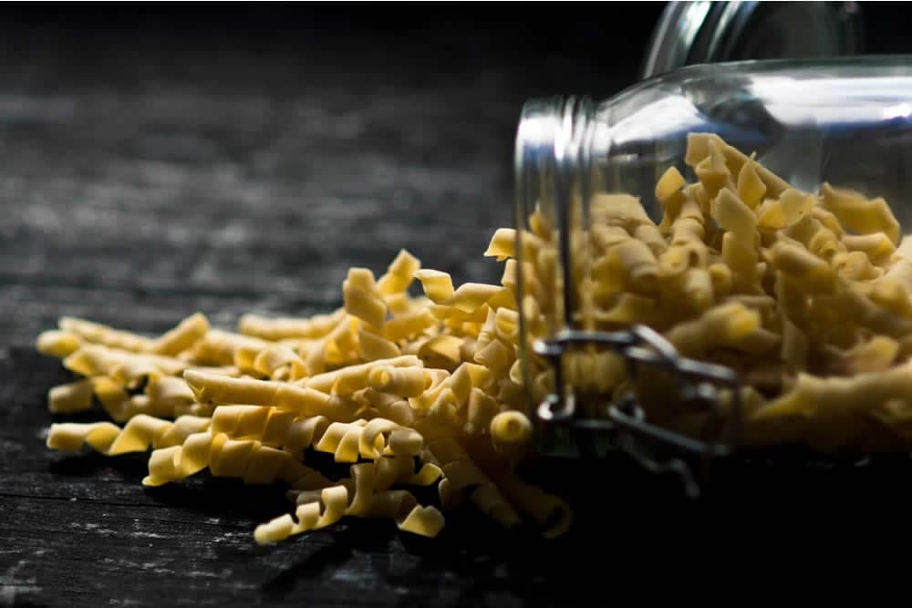 A mason jar spills uncooked pasta onto a dark surface.