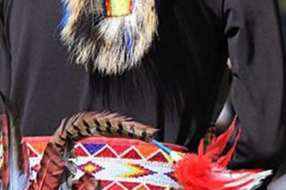 A person wearing traditional attire with colorful beadwork and feathers on the back.