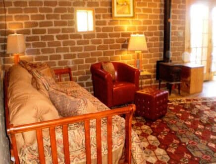 Cozy room featuring a wooden daybed, red armchair, and decorative rug against a brick wall.