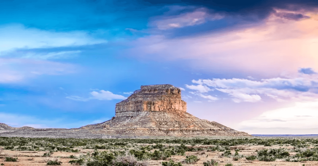 A rocky mesa rises against a colorful sky with scattered clouds.